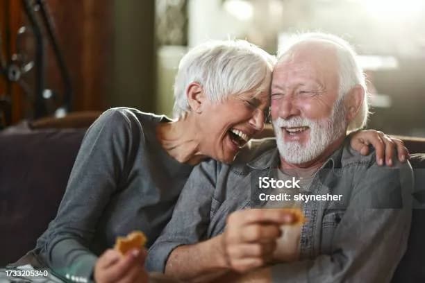An older couple laughing together on their sofa at home